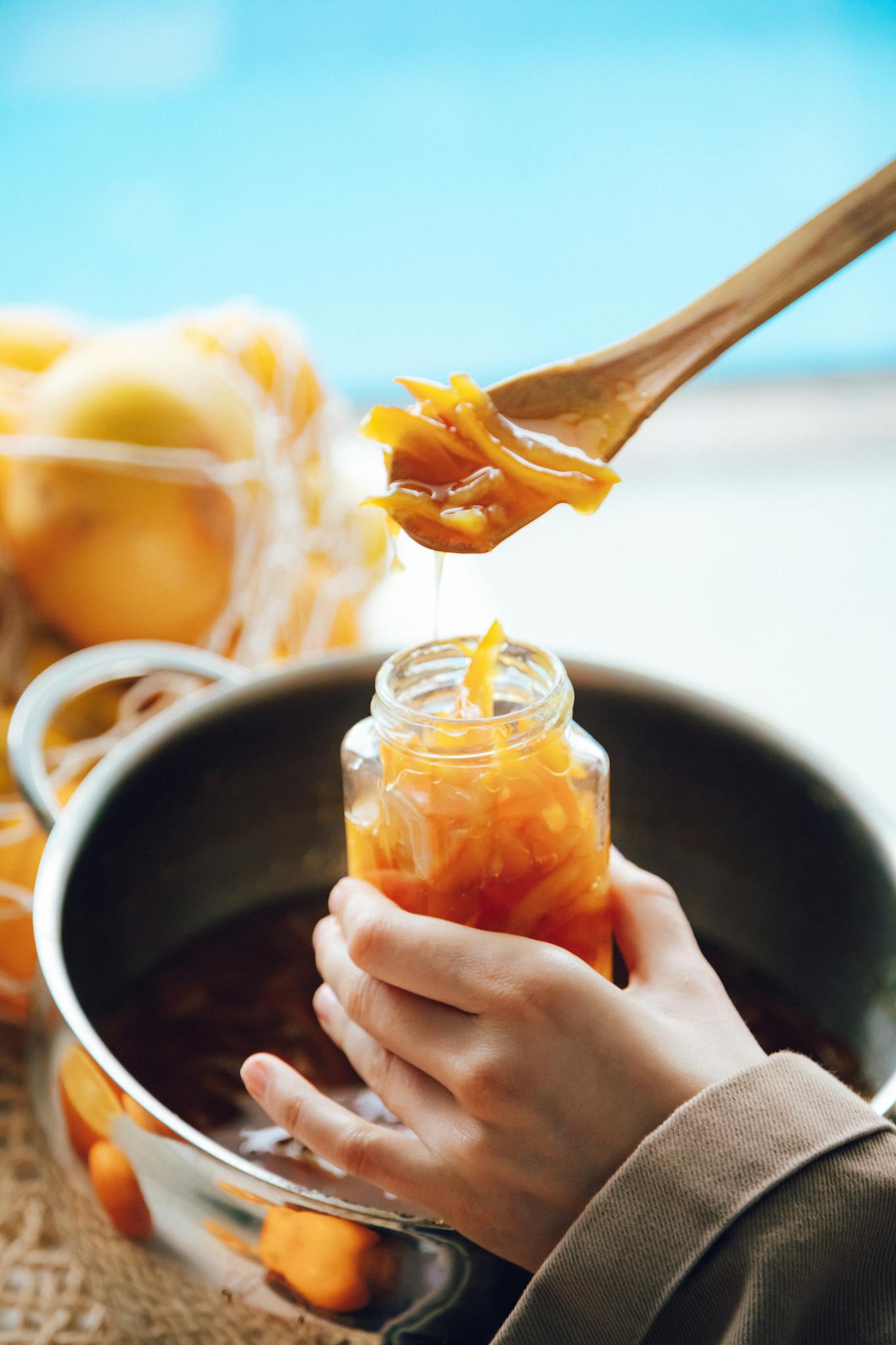 Close-up of homemade orange marmalade being spooned into a glass jar in a kitchen setting.